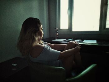 Rear view of woman sitting by window at home