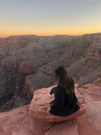 Rear view of woman sitting on rock against sky