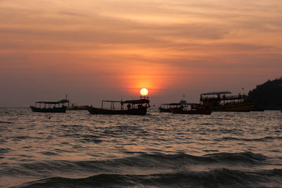 Silhouette boats in sea against orange sky