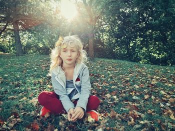 Portrait of cute girl sitting on grassy land in park during autumn