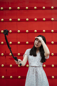 Full length of smiling young woman standing against red wall