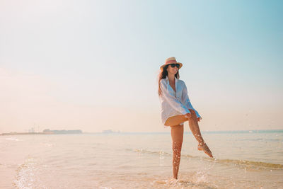 Full length of young woman standing at beach against sky