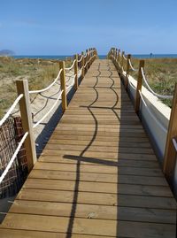 Wooden footbridge leading towards sea against sky