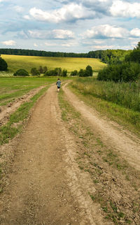 Rear view of teenage girl walking on field against sky