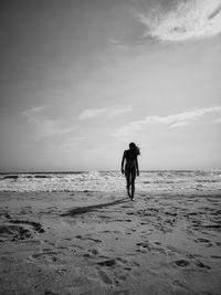 Rear view of woman walking at beach against sky