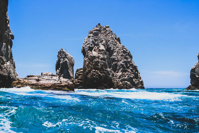 Rock formation in sea against clear blue sky