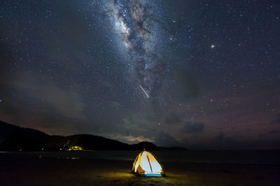 Illuminated tent at beach against sky at night