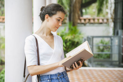 Woman reading book while standing by column