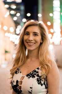 Portrait of smiling young woman against illuminated lights