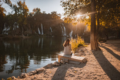 Rear view of man sitting on bench by lake