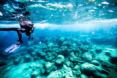 Close-up of scuba diver swimming over rocks undersea