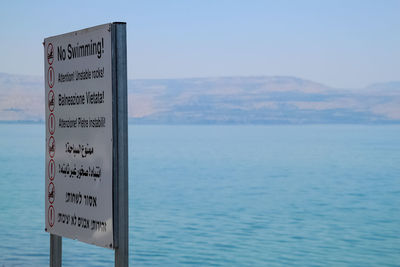 Information sign by sea against sky