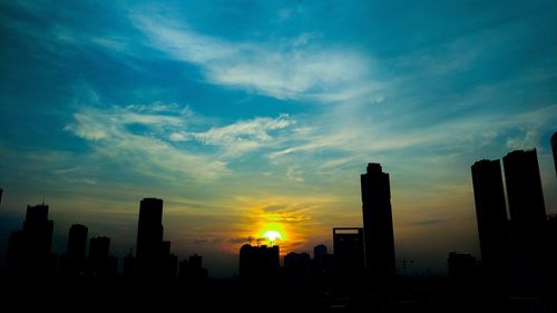 Silhouette of city against cloudy sky during sunset