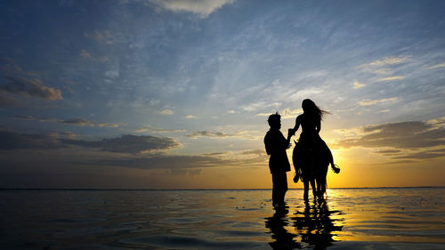 Silhouette women on beach against sky during sunset