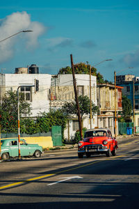 Cars on city street by buildings against sky