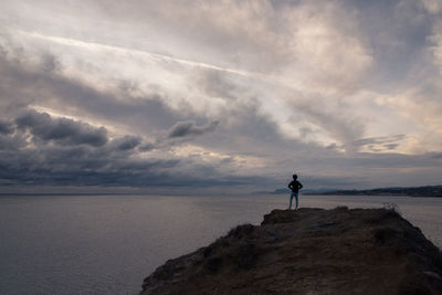 Rear view of teenager boy standing by cliff against sea and sky