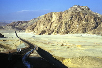 Vehicles on road by mountain against clear sky