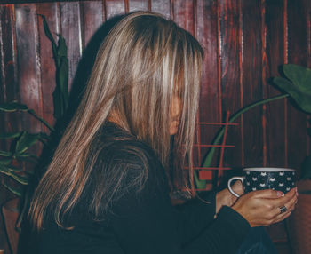 Side view of woman holding coffee cup sitting at cafe