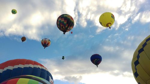 Low angle view of hot air balloons flying against cloudy sky