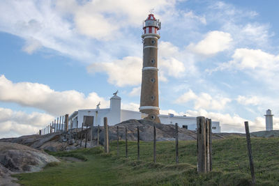 Lighthouse on field by historic building against sky