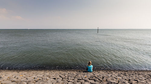 Rear view of woman sitting on beach against sky