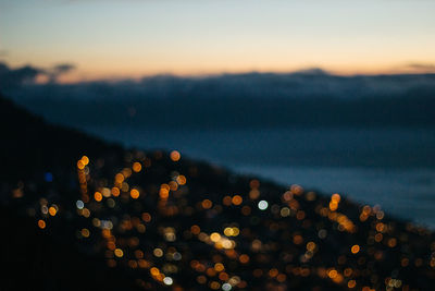 Defocused image of illuminated lights against sky at night