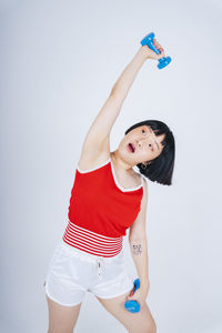 Young woman exercising with dumbbell against gray background