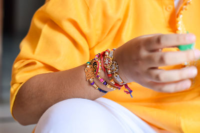 Midsection of boy wearing rakhis while sitting at home