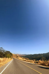 Empty road against clear blue sky