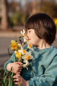 Cute little toddler boy enjoying smelling spring white and yellow daffodils outdoors in garden.