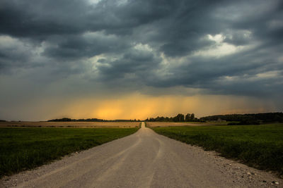 Road amidst field against storm clouds