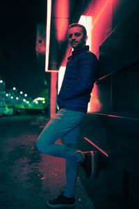 Portrait of young man standing on footpath against building at night