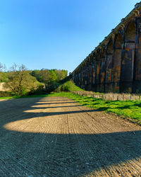 Road by trees against blue sky on sunny day