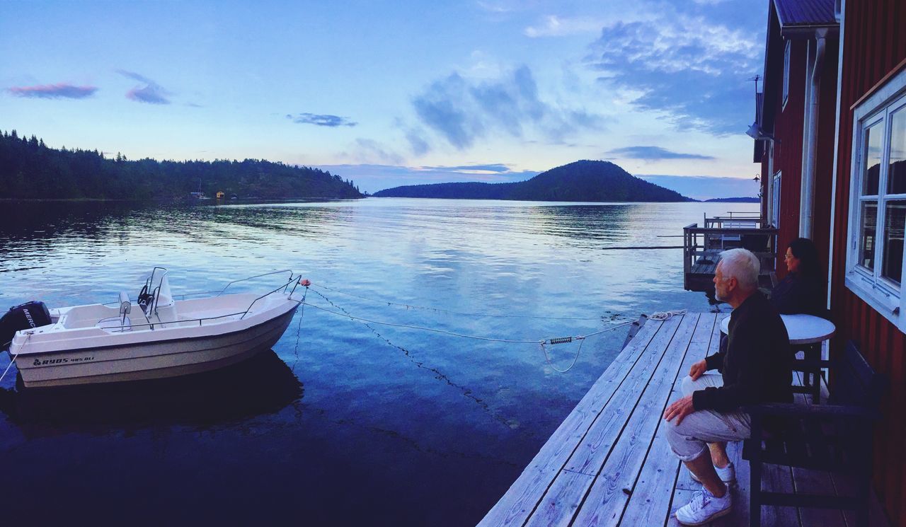 nautical vessel, real people, sky, water, nature, one person, transportation, outdoors, moored, full length, lake, rear view, cloud - sky, day, sitting, scenics, men, beauty in nature, leisure activity, tranquility, mountain, lifestyles, tree, people