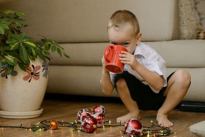 Portrait of boy having drink while crouching by illuminated string light during christmas