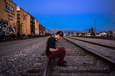 Man sitting on railroad track against clear sky