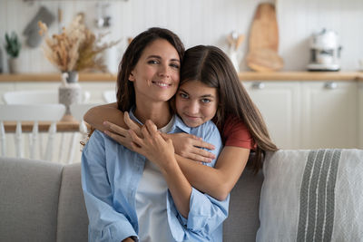 Mother-daughter connection. cute girl child cuddling smiling mom, sitting together on sofa at home