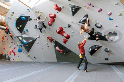 Male trainer training woman and man in wall climbing at gym