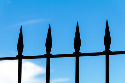 Low angle view of silhouette fence against blue sky