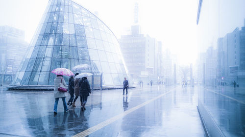 People walking on street by buildings during rainy season