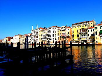 Buildings by canal against clear blue sky in city