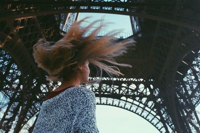 Rear view of young woman with tousled hair standing below eiffel tower