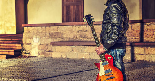 Midsection of man holding guitar standing outdoors