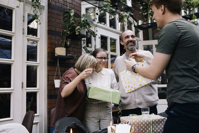 Side view of man giving gift to sister while standing at restaurant