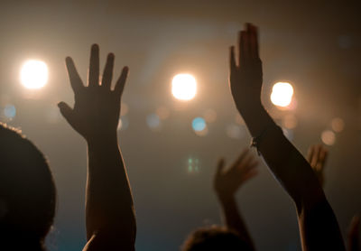 Cropped hands of people against illuminated lights in concert