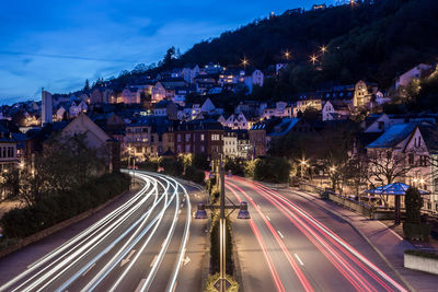 Light trails on street by buildings against sky at dusk