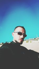 Portrait of young man wearing sunglasses standing against clear sky