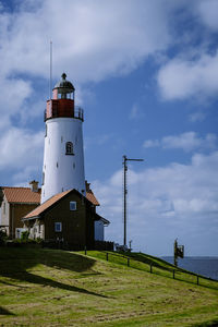 Lighthouse on field by building against sky