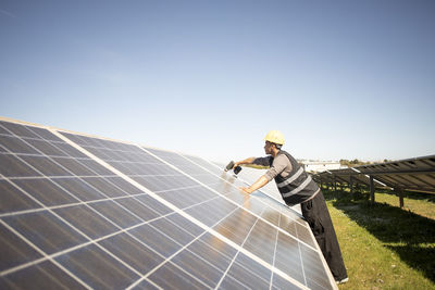 Side view of male engineer drilling on solar panels while working at power station