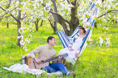 Man playing guitar while woman sitting on hammock at park